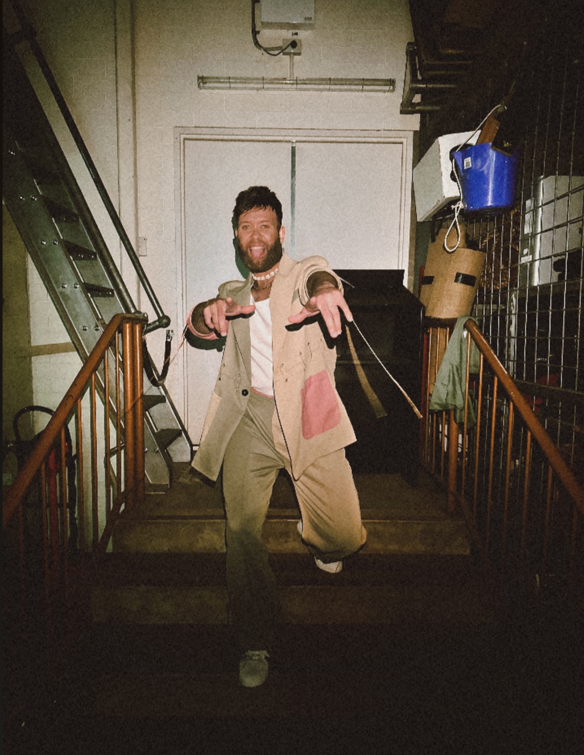 Performer Garret Lyon stands on a staircase, pointing to the camera.